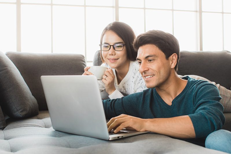 Caucasian businessman and Asian businesswoman wearing casual dress sitting together in living room and working on laptop notebook computer with relax and happiness. Idea for modern working at home